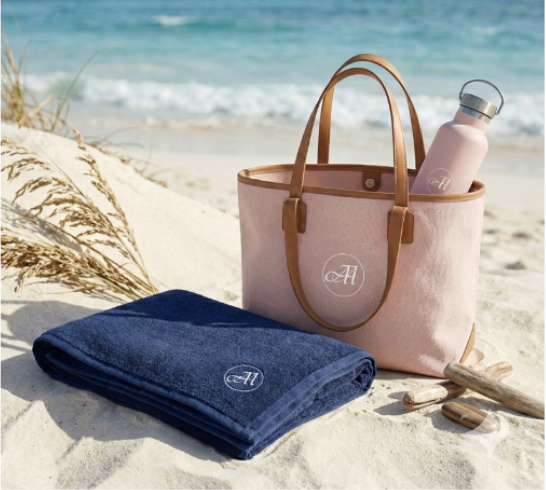 Aphrodite Atelier complimentary gift — blush tote bag, water bottle and navy blanket on a sandy beach